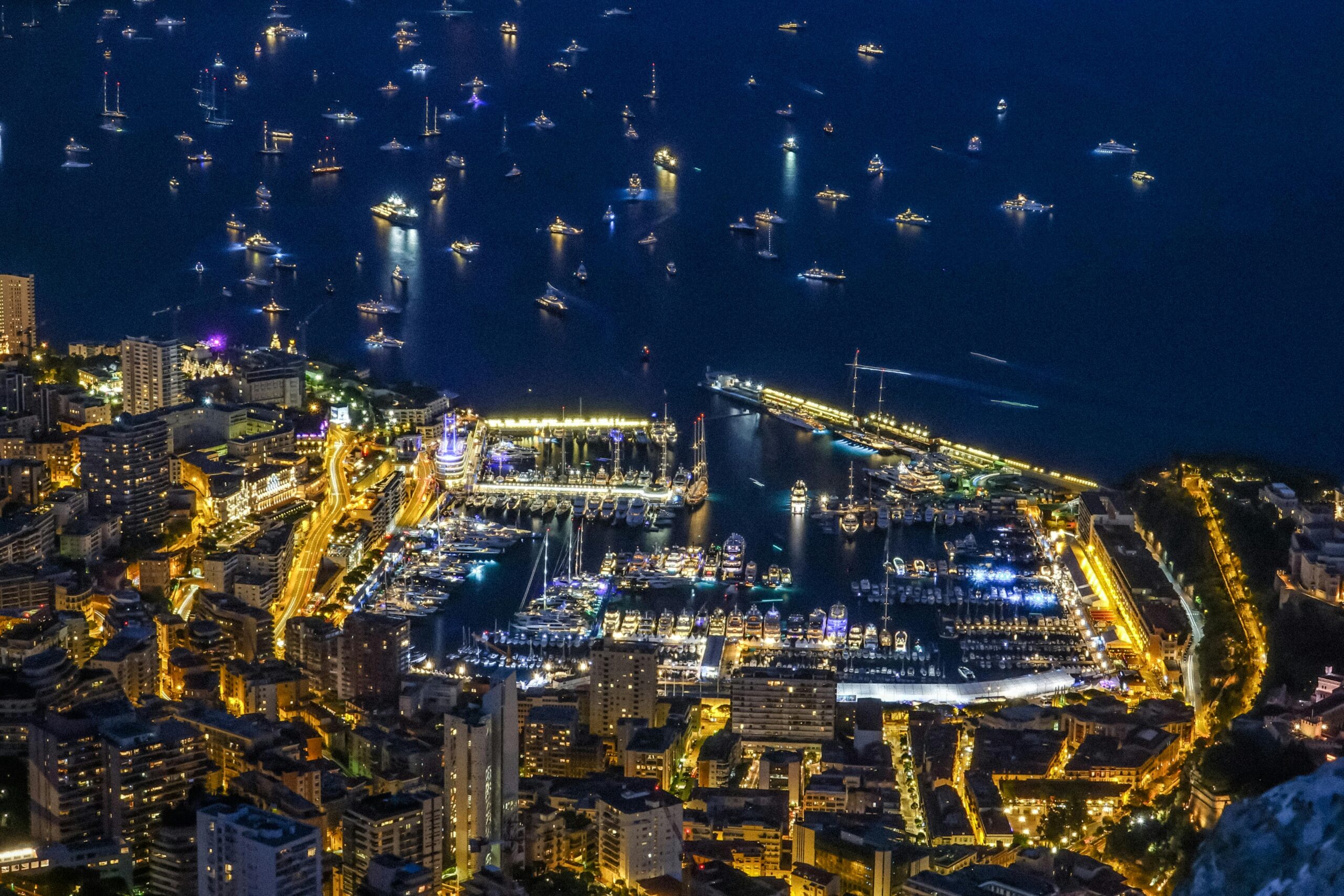 A breathtaking aerial night view of Monaco's illuminated harbor with numerous yachts.